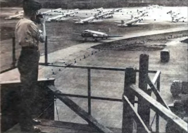 Разгар перевозок по воздушному мосту. Диспетчер аэродрома RAF в Вуншторфе сигналит Дакоте, осуществляющей рулежку.
